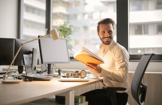 Smiling man with a book with a workstation